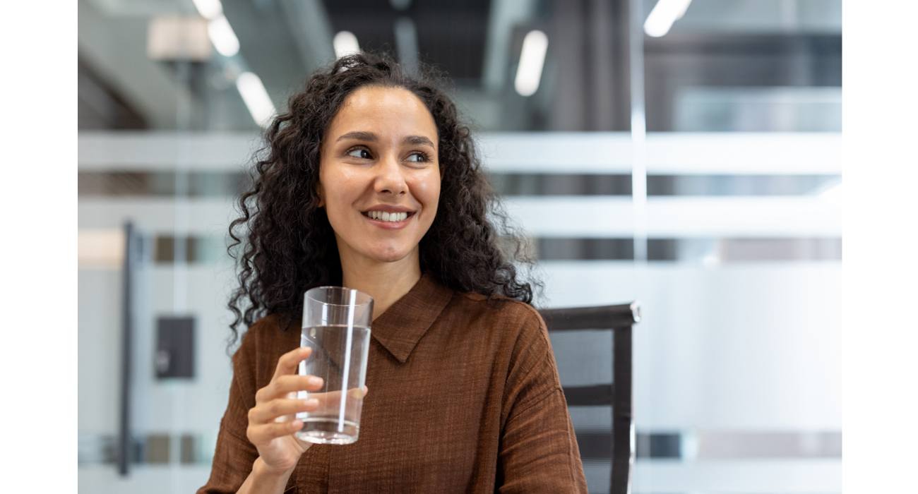 Woman drinking from water glass in office smiling Woman drinking from water glass in office smiling