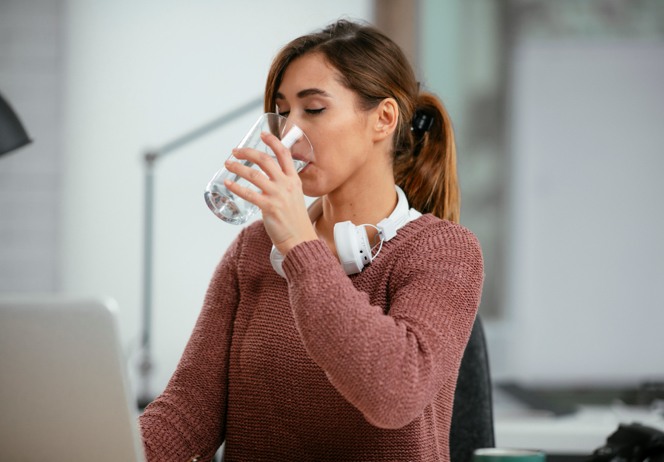 Woman drinking water from office water dispenser.